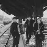 Die Gruppe vinorosso, bestehend aus drei Männer, steht an einem Bahnhof. Werbefoto.